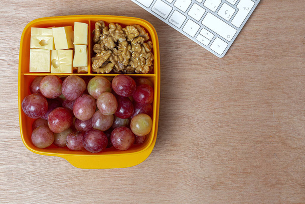 Gezond eten in plastic containers klaar om te eten met kaas, druiven en walnoten op de werktafel. Om walnoten mee te nemen.Walnoten - Foto, afbeelding