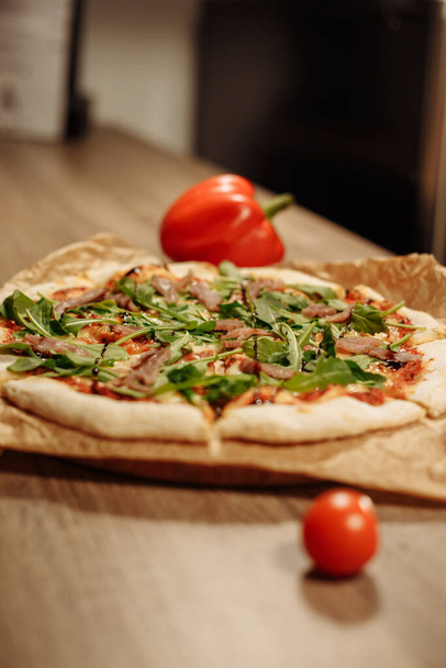 świeża pizza z ziołami, tuńczykiem i sosem balsamicznym na papierze spożywczym na drewnianym stole w przytulnej kawiarni, papryka w tle - Zdjęcie, obraz
