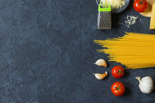 Food frame. Pasta ingredients. Cherry tomatoes, spaghetti pasta, garlic, basil, parmesan and spices on a dark grunge background, copy space, top view. Horizontal position. - Foto, Imagem