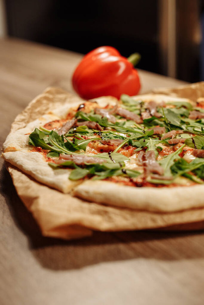 frische Pizza mit Kräutern, Thunfisch und Balsamico-Soße auf Esspapier auf einem Holztisch in einem gemütlichen Café, Paprika im Hintergrund - Foto, Bild