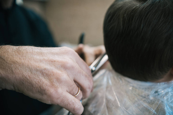 Невпізнаваний чоловік, який ріже і розчісує волосся дитини і дитини в перукарні з ножицями і гребінцем
 - Фото, зображення