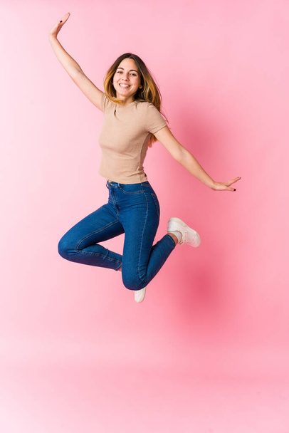 Молода біла жінка стрибає на рожевому фоні
 - Фото, зображення