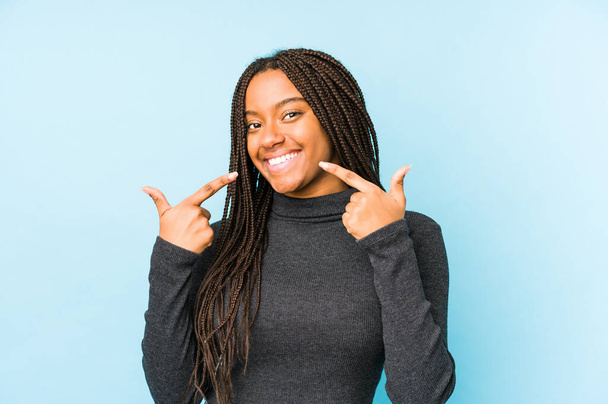 Young african american woman isolated on blue background smiles, pointing fingers at mouth. - Foto, Imagem