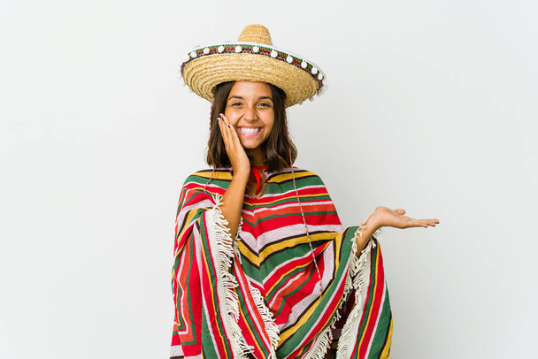 Jeune femme mexicaine isolée sur fond blanc tient l'espace de copie sur une paume, garder la main sur la joue. Incroyable et ravi. - Photo, image