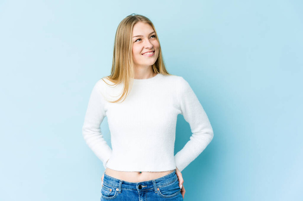 jonge blonde vrouw geïsoleerd op blauwe achtergrond ontspannen en gelukkig lachen, nek gestrekt tonen tanden. - Foto, afbeelding