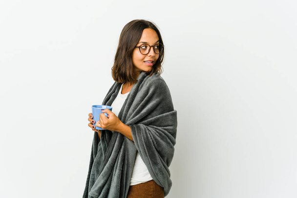 Young latin woman with blanket isolated on white background looks aside smiling, cheerful and pleasant. - Valokuva, kuva
