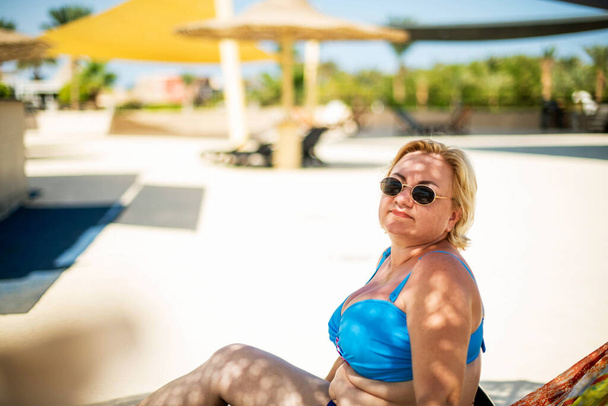 Fröhliche Plus-Size-Frau mit Sonnenbrille genießt am Pool. lächelnd, glücklich, positive Emotionen, sommerlicher Stil. Glück und schöner Körper für einen alternativen Lebensstil als Urlaub - Foto, Bild