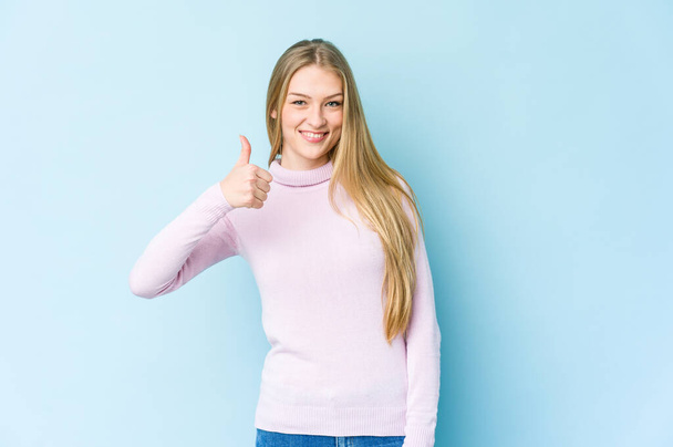 Young blonde woman isolated on blue background smiling and raising thumb up - Foto, immagini