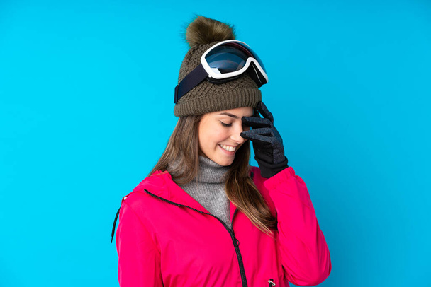 Дівчина-підліток лижниця зі сноубордистськими окулярами над ізольованим синім фоном сміється
 - Фото, зображення