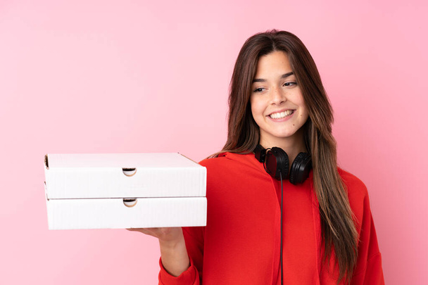 Teenager Brazilian girl holding pizza boxes over isolated pink wall with happy expression - Foto, imagen