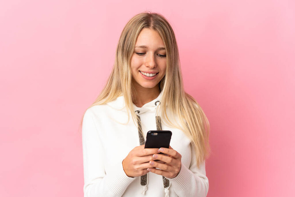 ピンクの背景に隔離された若いブロンドの女性携帯電話でメッセージや電子メールを送信 - 写真・画像