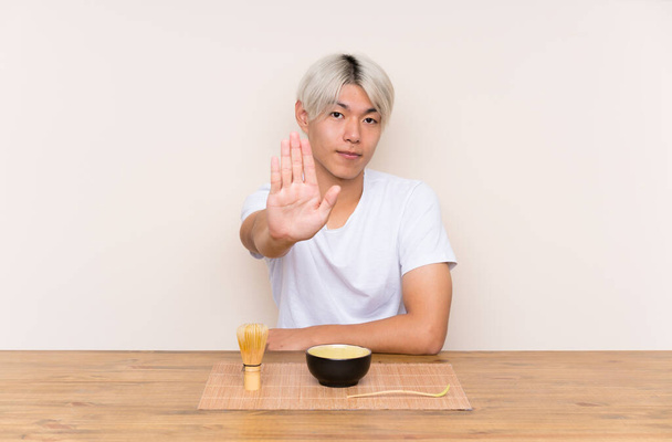 Молодий азіатський чоловік з чаєм мача в столі робить стоп жест своєю рукою
 - Фото, зображення