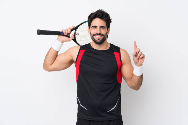 Молодой красивый мужчина с бородой на изолированном белом фоне играет в теннис и указывает вверх - Фото, изображение