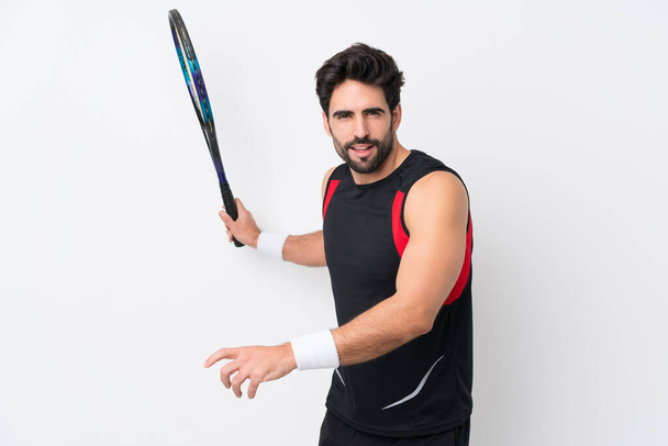Joven hombre guapo con barba sobre fondo blanco aislado jugando tenis - Foto, Imagen