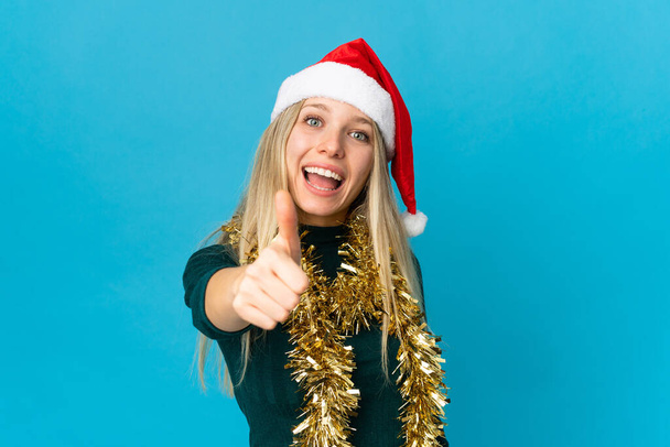 Woman with christmas hat isolated on blue background with thumbs up because something good has happened - Фото, зображення