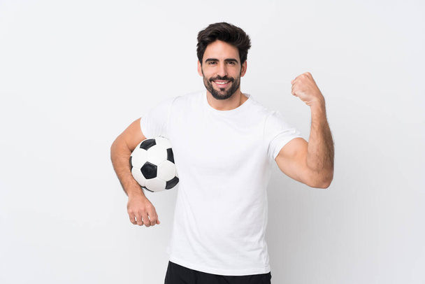 Молодой красивый мужчина с бородой на изолированном белом фоне с футбольным мячом празднует победу - Фото, изображение