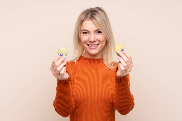 Young blonde Russian woman over isolated background offering colorful French macarons - Foto, Imagem