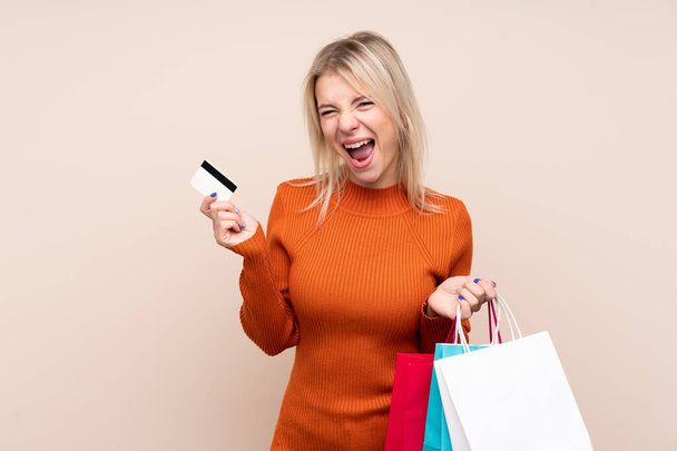 Mladá blondýna žena přes izolované pozadí držení nákupních tašek a kreditní karty - Fotografie, Obrázek