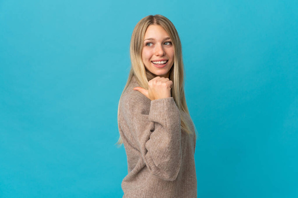 Junge blonde Frau isoliert auf blauem Hintergrund zeigt auf die Seite, um ein Produkt zu präsentieren - Foto, Bild