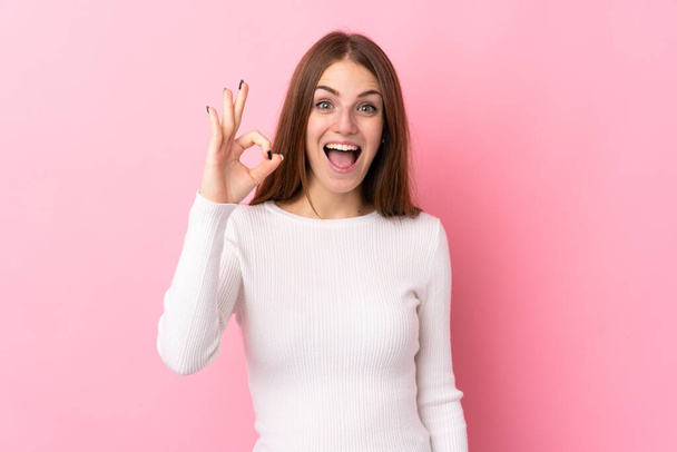 Young woman over isolated pink background surprised and showing ok sign - Foto, afbeelding