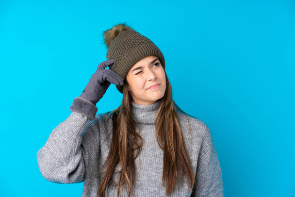 Teenager girl with winter hat over isolated blue background having doubts and with confuse face expression - Photo, Image