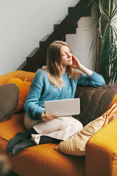 Menina bonita Pensive sentado no sofá com um laptop. Jovem mulher trabalhando em casa usando laptop - Foto, Imagem