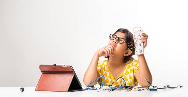 electronic experiment - Asian Indian small girl student performing or studying science with wires, connections, studying from laptop or tablet computer - Foto, afbeelding