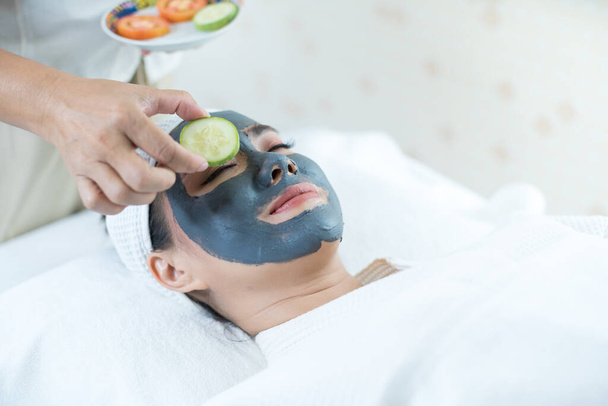 Young woman doing skin spa using mud and fruit in spa shop. Facial spa. - Photo, Image