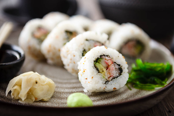 Sushi maki rollos de California con cangrejo, pepino y aguacate en un plato con palillos, salsa de soja, wasabi y jengibre. Marisco tradicional japonés servido para el almuerzo en el restaurante gourmet moderno. - Foto, imagen