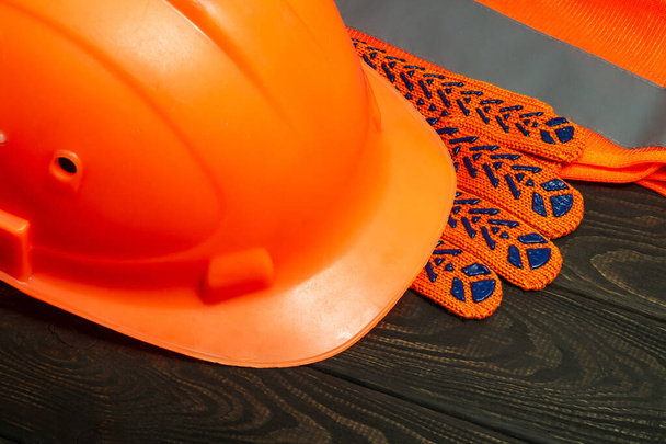Оранжевое защитное оборудование мастера-строителя, сложенное на черных досках до войны - Фото, изображение