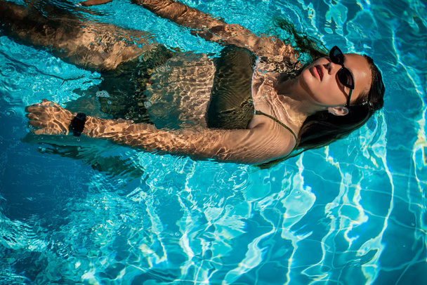 Retrato de moda de la elegante chica linda en gafas de sol elegantes posando en la piscina durante las vacaciones en el complejo de lujo. Alegre más tamaño adolescente disfrutando. feliz, emoción positiva, estilo de verano. - Foto, Imagen