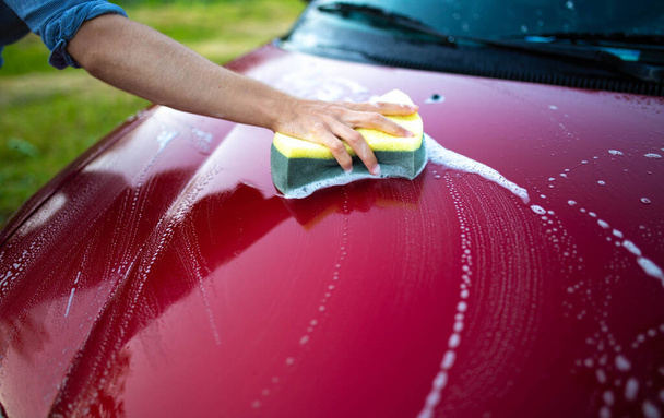 rotes Auto mit Händen und Schwamm waschen, den Lack pflegen. - Foto, Bild