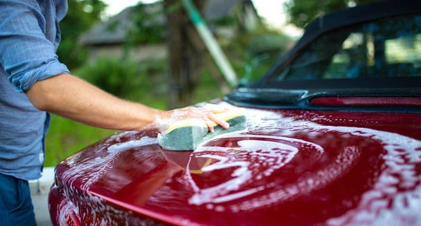 male hands and a sponge washes a red car, care of a varnish with a colorful coating. - 写真・画像