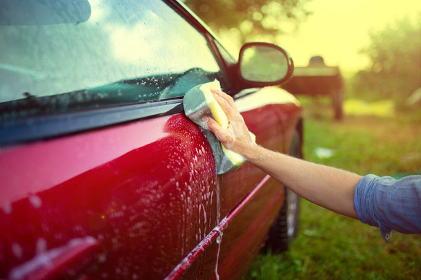 washing a red car with hands and a sponge, caring for the paintwork. - Фото, изображение
