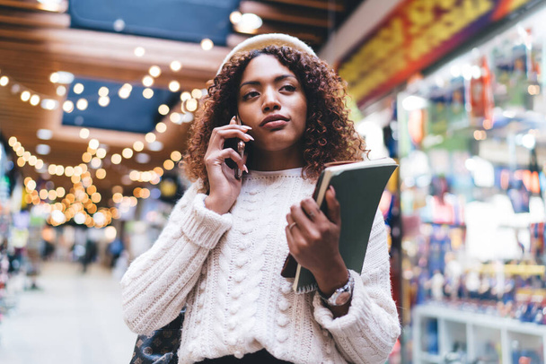 Piękna, ciemnoskóra kobieta w modnym stroju na zewnątrz rozmawiająca przez telefon komórkowy za pomocą taniej taryfy, atrakcyjna, afrykańska kobieta millenialska rozmawiająca na smartfonie za pomocą roamingu międzynarodowego - Zdjęcie, obraz