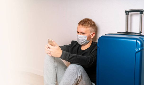 A man in a medical mask holds Russian passports and sits next to Luggage at the airport. The concept of travel during the coronavirus e - Photo, image