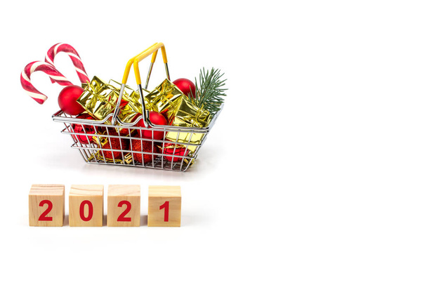 kleine boodschappenmand gevuld met kerstcadeaus geïsoleerd op witte achtergrond. houten kubussen uit 2021 tekst. Cristmas shopping concept. kopieerruimte - Foto, afbeelding