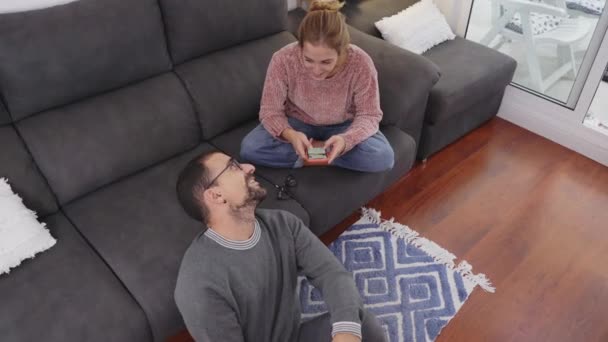 Draufsicht auf ein glückliches junges Paar, das entspannt mit Kaffeetassen plaudert und auf der Couch im Wohnzimmer miteinander telefoniert. - Filmmaterial, Video