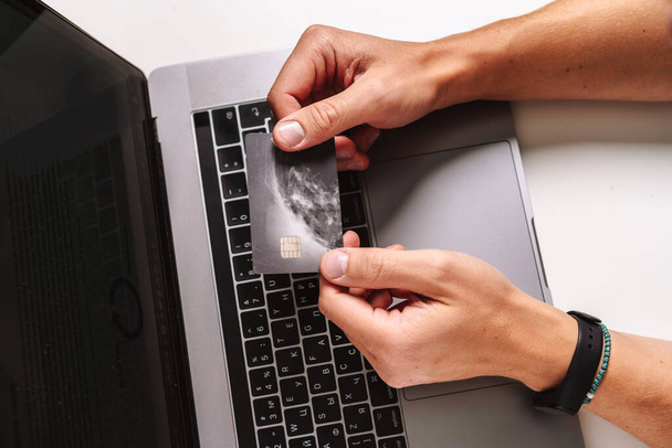Mężczyzna trzyma plastikową kartę kredytową i używa laptopa. Koncepcja zakupów online. - Zdjęcie, obraz