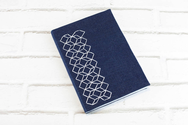 Голубая тетрадь ручной работы с вышитым чехлом из ткани с шестиугольниками и белой нитью на кирпичном фоне - Фото, изображение