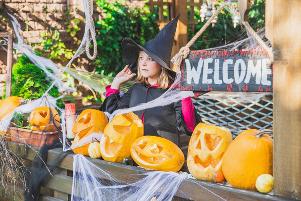 menina em um manto e um chapéu fica perto das abóboras de Halloween - Foto, Imagem