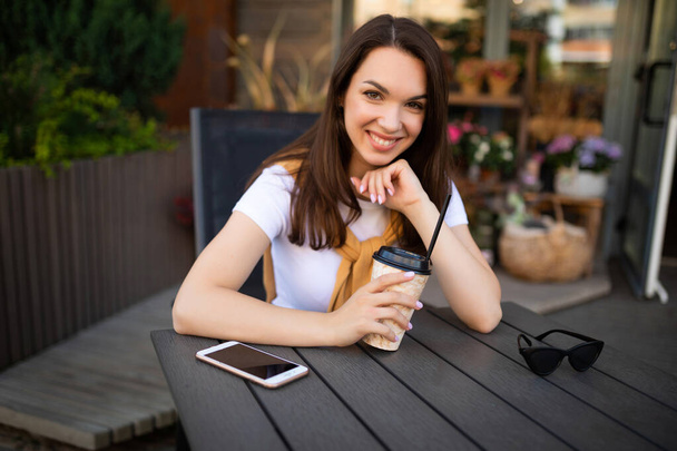 smiling young woman freelancer drinking coffee on cafe terrace - Foto, Bild
