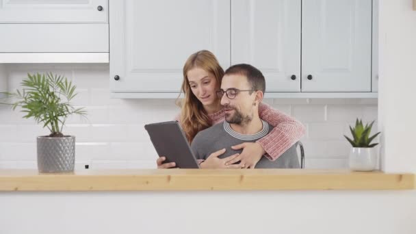 Couple lisant une tablette et riant dans la cuisine à la maison. - Séquence, vidéo
