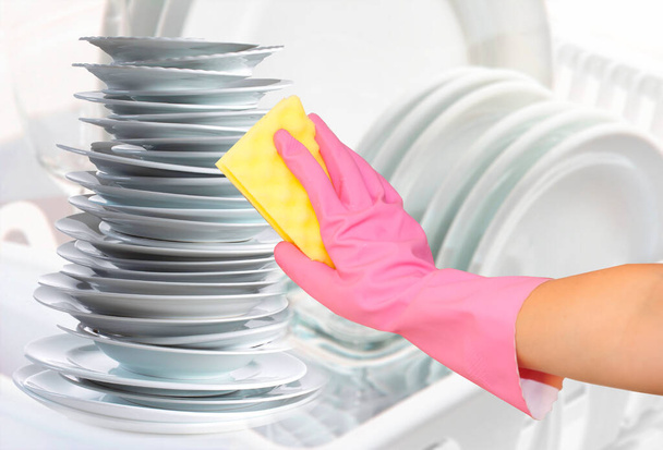 home dishwashing. cleaning plates and kitchenware using sponge and gloves. cleaning the kitchen and kitchenware. hand in pink glove with yellow sponge has being cleaned off kitchen, plate, range, pan, casserole, stove - Photo, Image