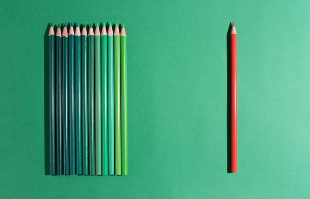 One red pencil lies in front of several green ones on a green background. - Foto, Bild