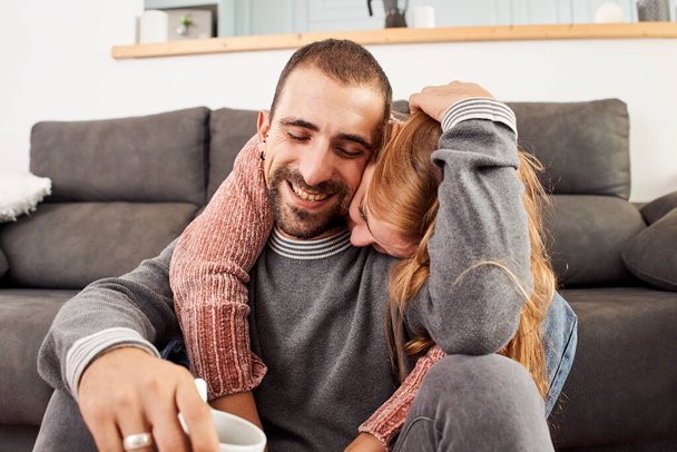 Feliz joven pareja relajándose hablando sosteniendo tazas de café en el sofá juntos en la sala de estar. - Foto, imagen