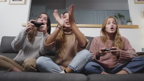 Vooraanzicht van een groep vrouwelijke vrienden die in de woonkamer op de bank zitten en thuis videospelletjes spelen. - Video