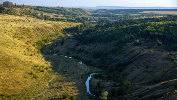 Nature de Moldavie, vallée avec rivière coulante, colline avec des arbres luxuriants sur la droite, pente avec végétation clairsemée sur la gauche, verdure au loin - Photo, image