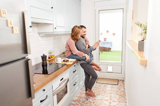 Glückliches junges Paar zu Hause in der Küche mit dem Handy - Foto, Bild