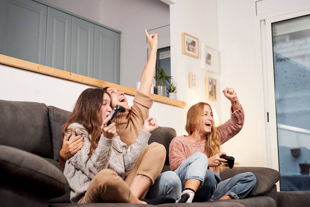 Gruppe von Freundinnen sitzt auf dem Sofa im Wohnzimmer und spielt zu Hause Videospiele. - Foto, Bild